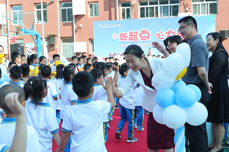 9月1日,“新起点-心力量”北京市海淀区中国农业科学院附属小学2023~2024学年第一学期开学典礼拉开帷幕。孩子们在班主任、副班老师和高年级哥哥、姐姐的引领下,经过缤纷绚丽的入学彩虹门,正式开启了精彩的小学生活。图为小学生和老师打招呼。北京市教委供图
